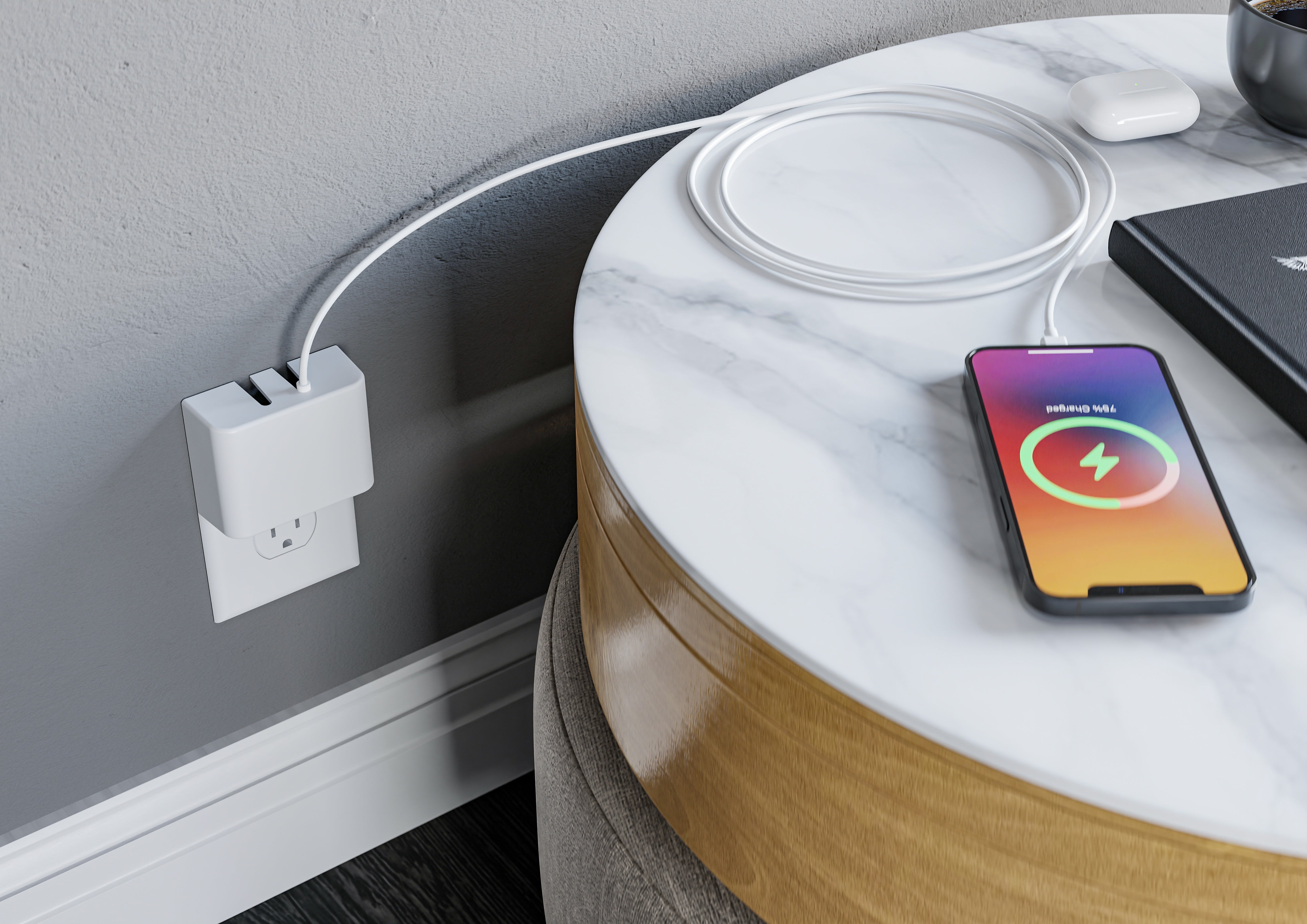 This image shows the Permaplug Charger Lock plugged into a wall outlet, powering both a smartphone and a pair of wireless headphones. The phone, placed on a round marble-top side table, displays a charging icon, indicating it is actively charging. The white charging cable is neatly coiled on the table, next to the wireless headphones and a closed laptop. The setup portrays a sleek and organized charging station in a modern environment.