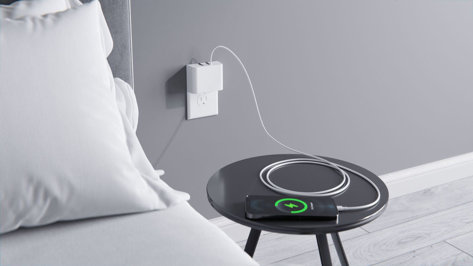 
This image shows the Permaplug Charger Lock plugged into a wall outlet next to a bed. The charger is powering a smartphone, which is placed on a nearby black side table and charging wirelessly. The cable is neatly coiled on the table, and the phone screen displays a green charging icon, indicating an active charge. The scene conveys a tidy and efficient bedside charging solution.